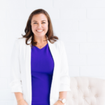 A woman wearing a purple dress and white blazer.
