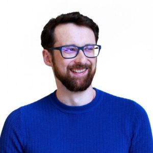 A bearded man wearing glasses and a blue sweater.