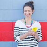A woman holding a cell phone in front of a red and blue wall.