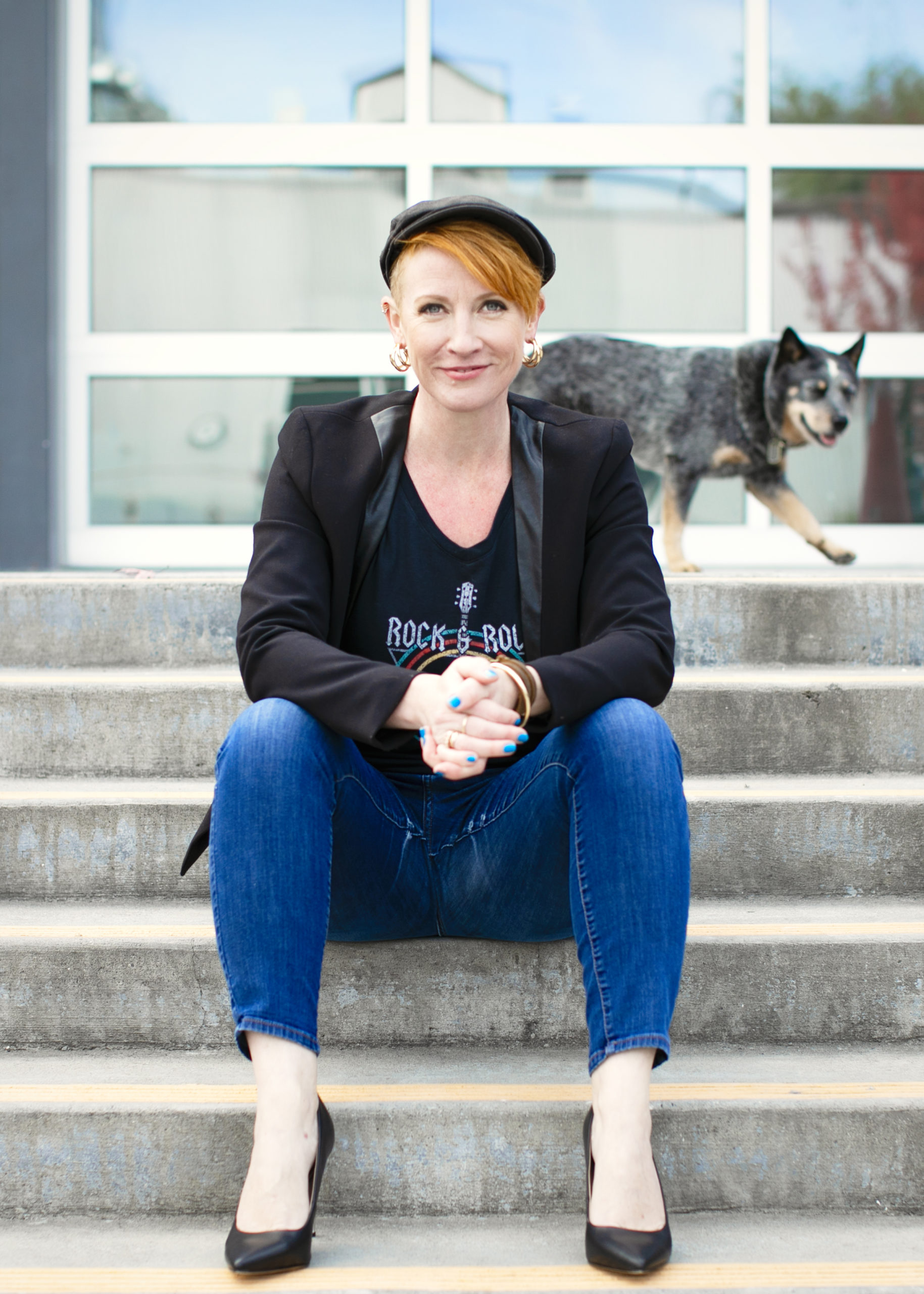 Copywriter Belinda Weaver sits on some stairs, looking chilled with dog walking behind her