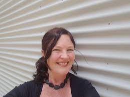 A woman smiling in front of a corrugated metal wall.