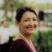 A smiling woman wearing a purple shirt and pearls.