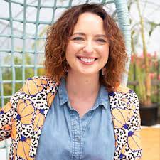 A woman with curly hair sitting on a swing in a garden.