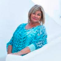 A woman in a blue dress leaning against a white wall.