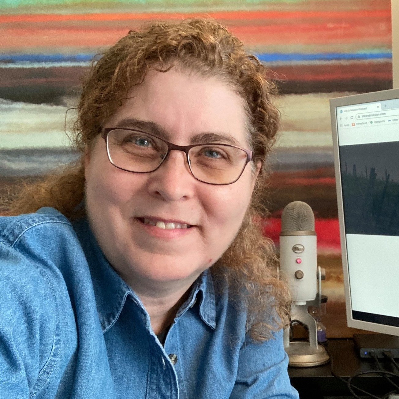 A woman with glasses smiling in front of a computer.