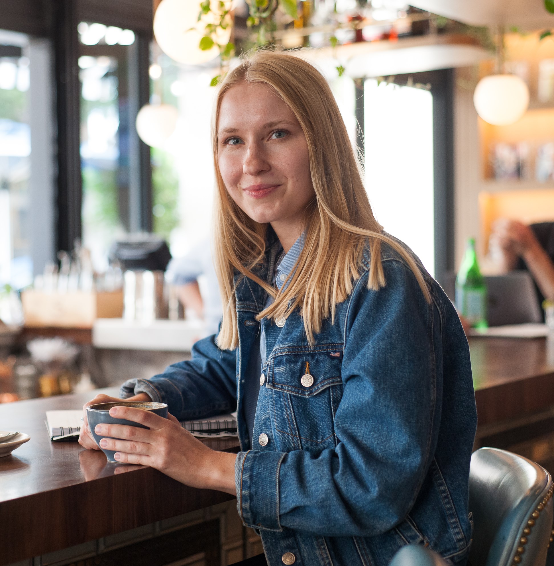 A woman in a denim jacket sitting at a bar.