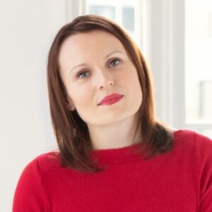 A woman in a red sweater standing in front of a window.