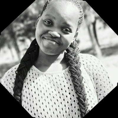 Smiling copywriter, Judith Awino, with braided hair, wearing a patterned top. Black and white photo with a nature background.