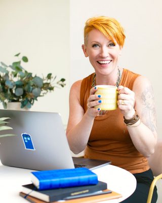 A woman sitting at a desk with a laptop and a cup of coffee.